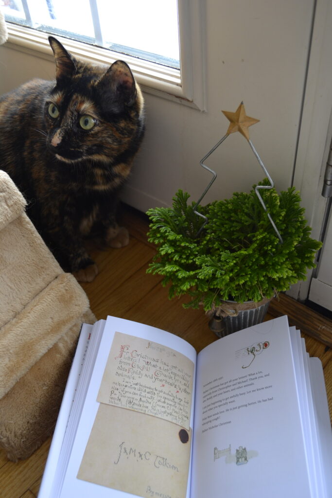 A tortoiseshell cat sits beside a frosty fern in a planter with a trellis shaped like a Christmas tree.