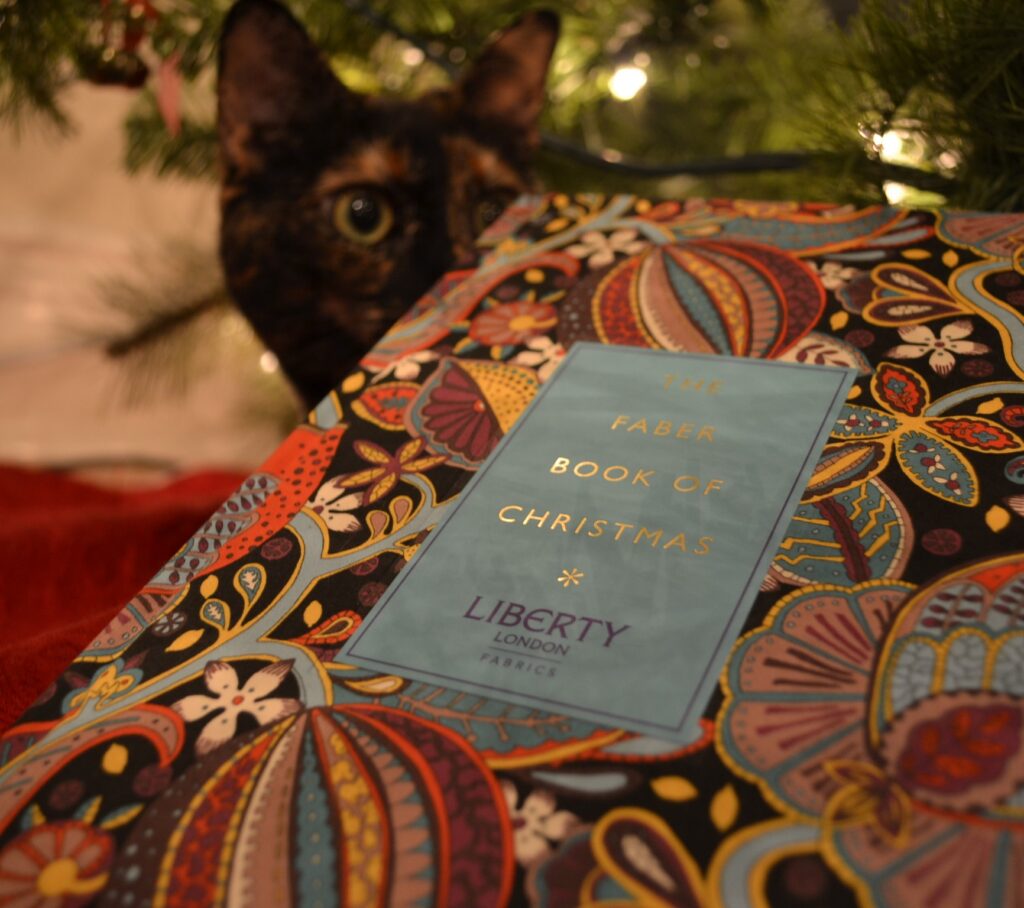 A tortoiseshell cat peeks over the corner of The Faber Book of Christmas.