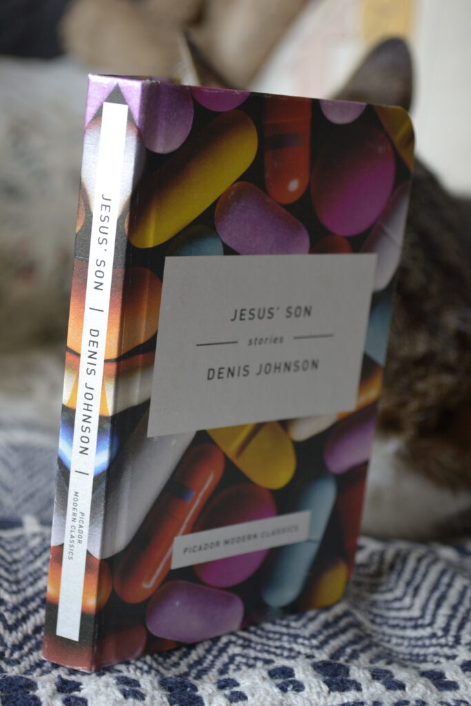 Jesus' Son by Denis Johnson is abook of short stories. This Picador Modern Classics edition is a pocket-sized hardcover with a picture of brightly coloured pills on the cover.