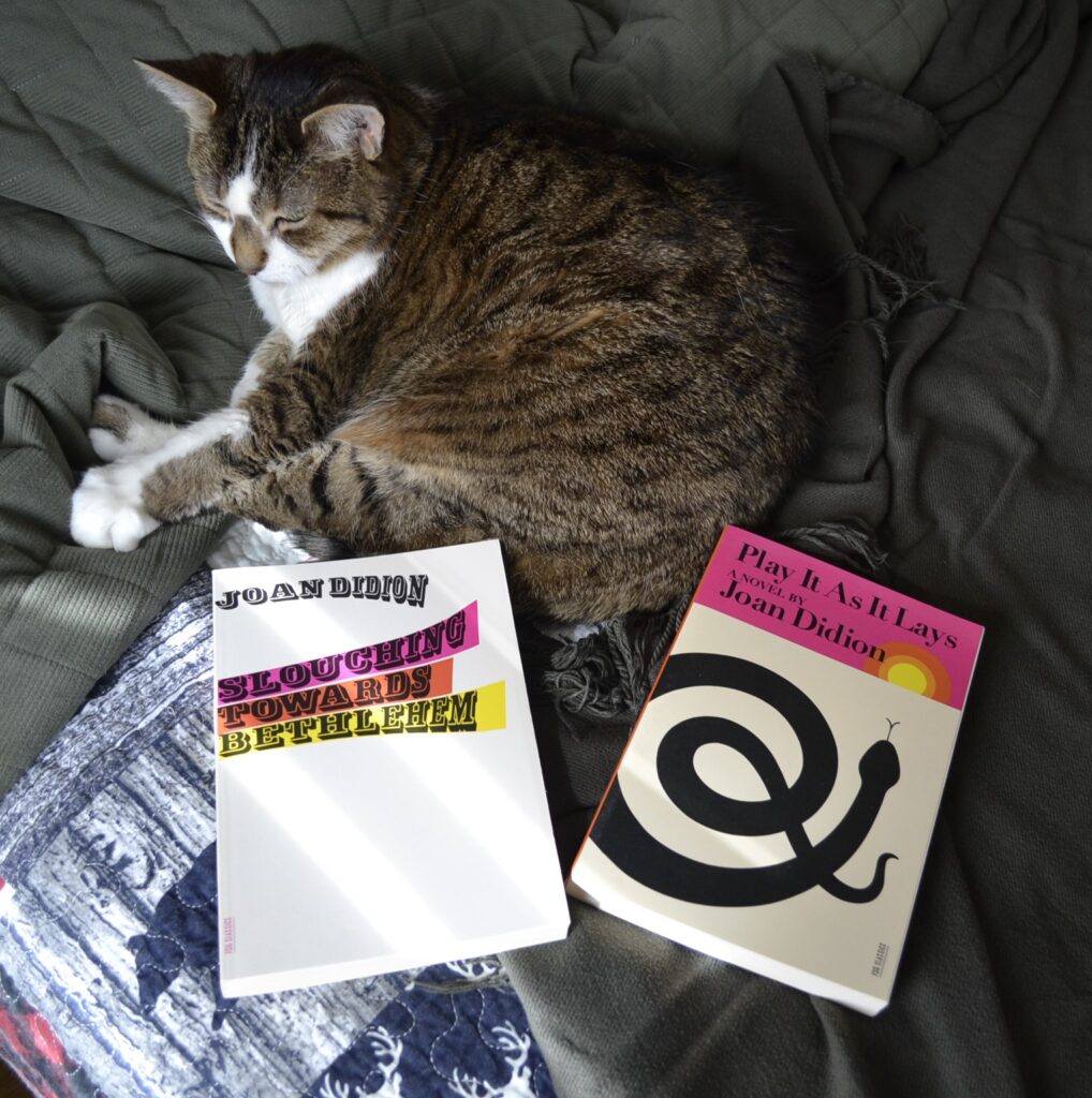A tabby cat lies curled between two books by Joan Didion.