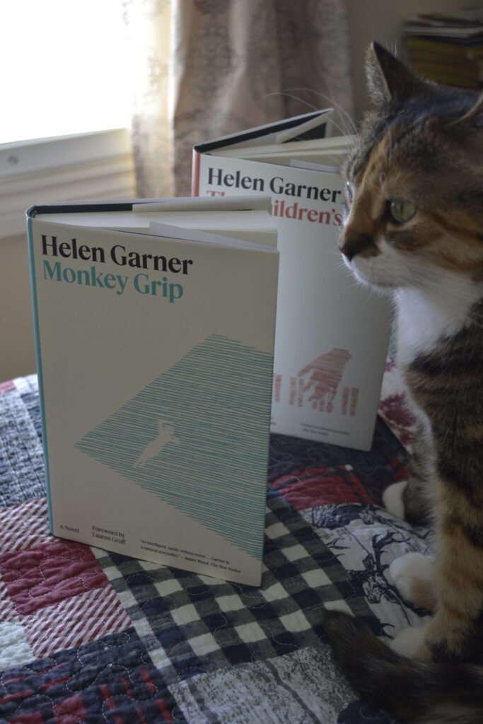 A calico tabby sits beside two books by Helen Garner: Monkey Grip and The Children's Bach.