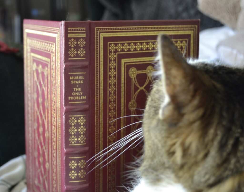 A cat looks at a red leatherbound edition of Muriel Spark's The Only Problem.