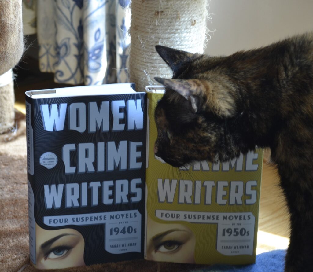 A tortie sniffs a pair of books: Women Crime Writers.