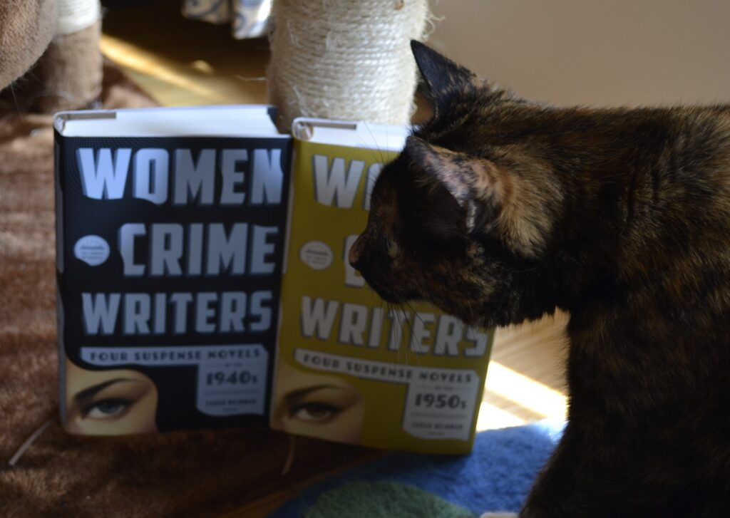 A tortie hunkers over two volumes of Women Crime Writers like a dark shadow.