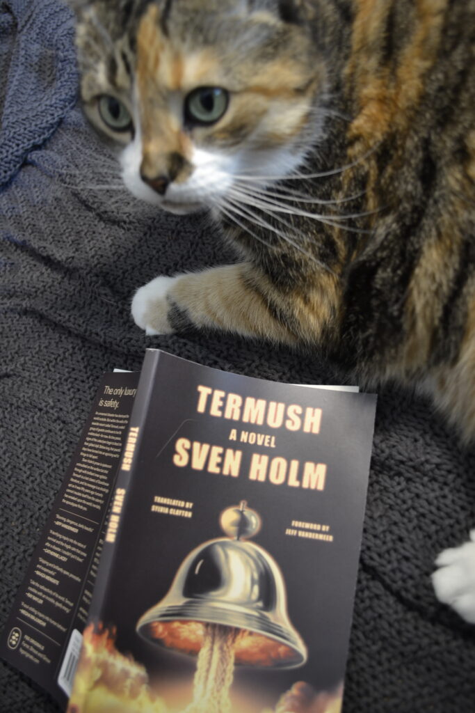 A calico tabby stands beside Termush by Sven Holm.