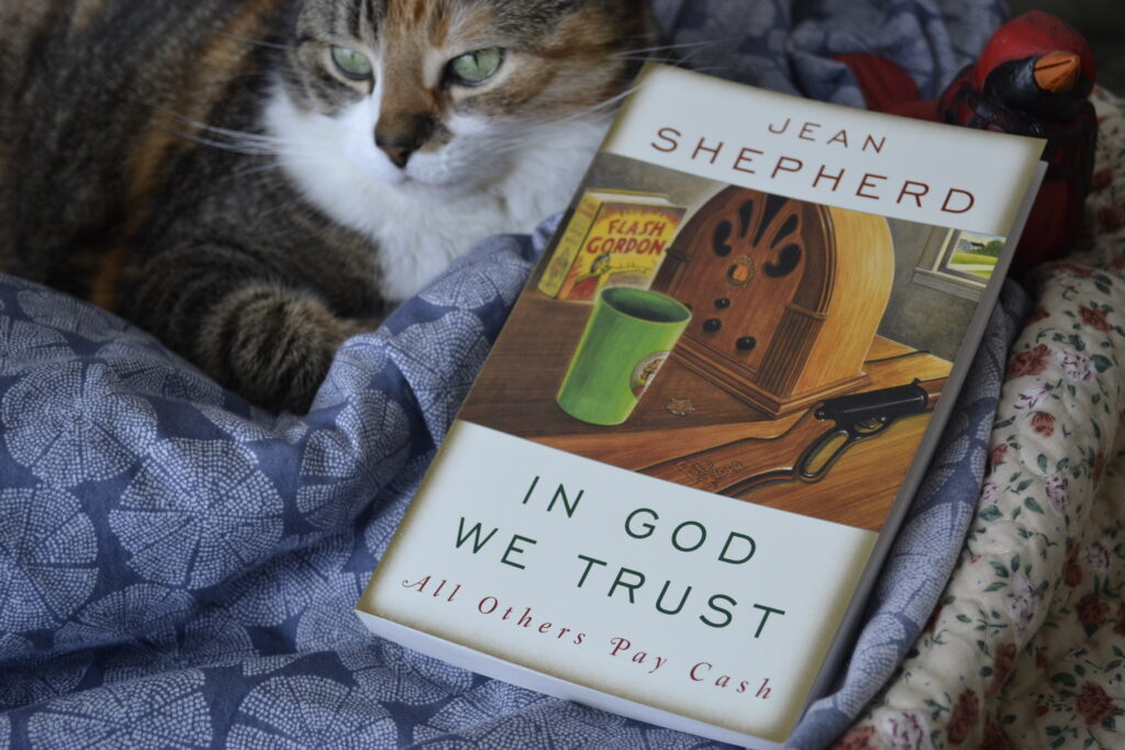 A calico tabby and a wooden cardinal lie beside a copy of In God We Trust.