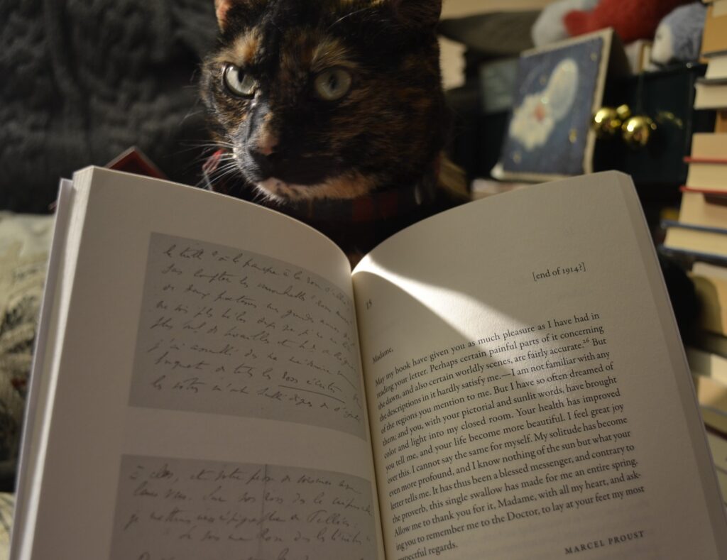 The inside of a slim book shows a letter signed 'Marcel Proust' and addressed to 'Madame'. Beside it is a picture of a letter handwritten in French.