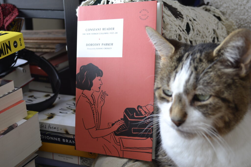 The Constant Reader, a red paperback book by Dorothy Parker, sits behind a tabby cat with big ears and green eyes.