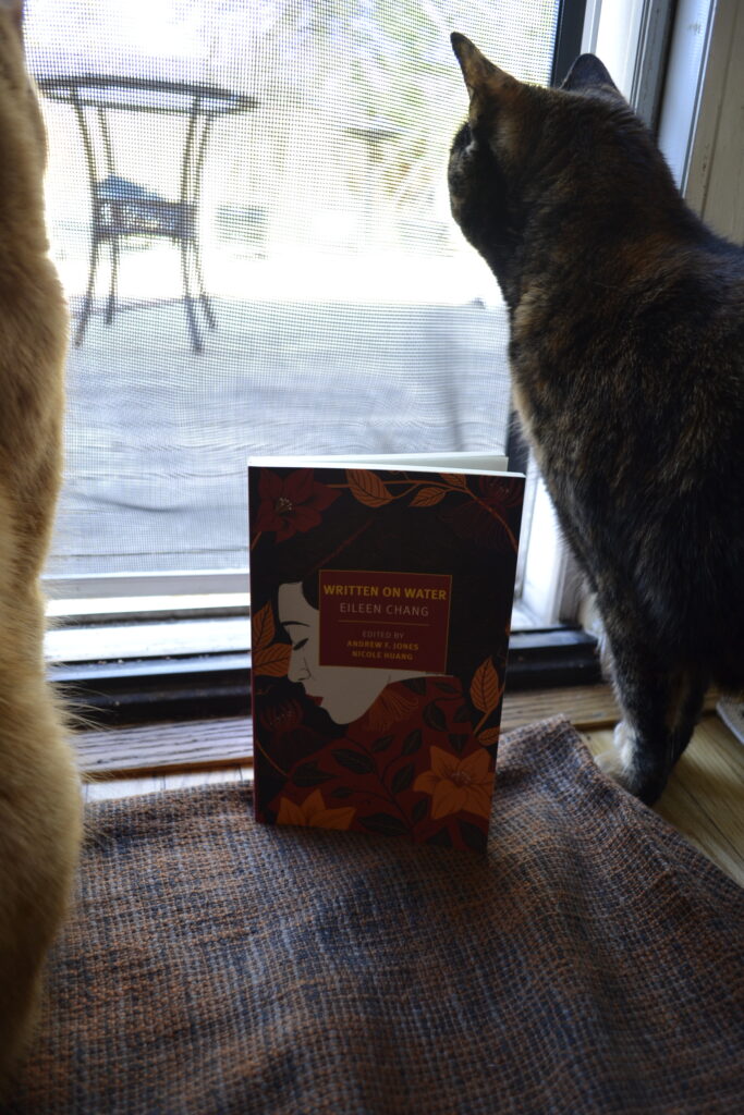 Written on Water by Eileen Chang is a paperback book. It features a woman with black hair, red lips, and a white face, wearing a red shirt and surrounded by orange and red flowers and vines.