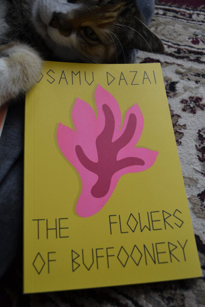 Osamu Dazai's The Flowers of Buffoonery is a yellow paperback book with a picture of a pink and red abstract cut-out that looks like either a flame or a flower.