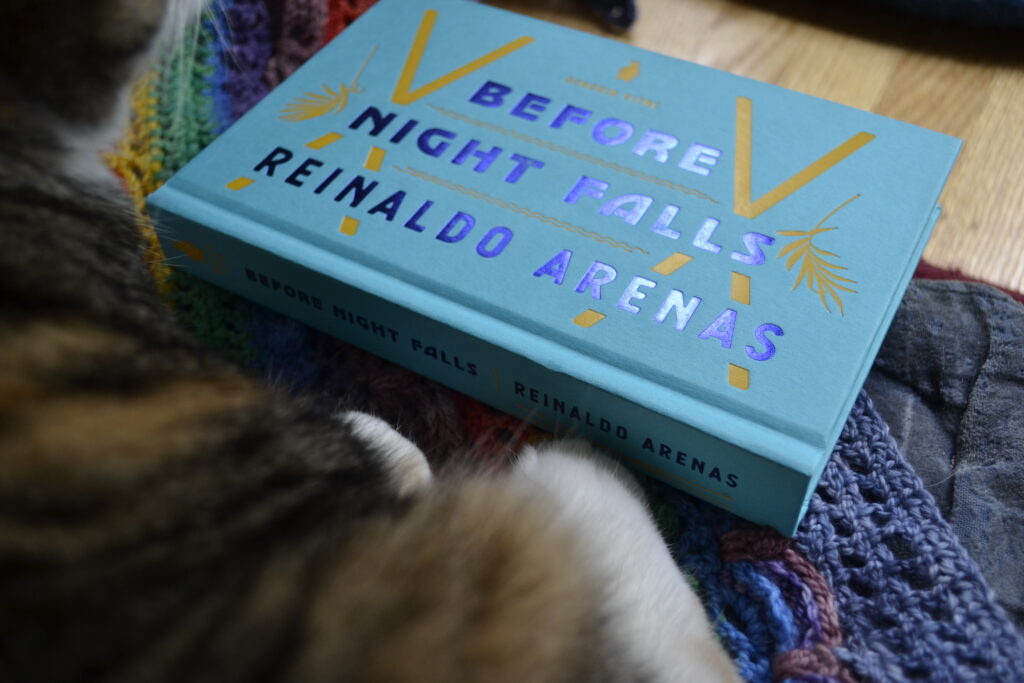 Before Night Falls by Reinaldo Arenas is a small bright blue hardcover. The title and author are set in dark blue foil lettering, and the details of X's and botanicals are in embossed yellow.