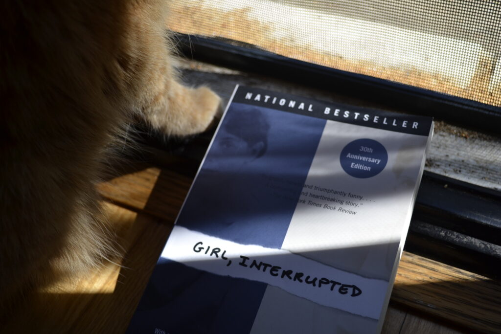 The cover of Girl, Interrupted by Susanna Kaysen has a picture of a woman, split through the middle of her face and reassemble so that one side of her face aligns with each edge of the cover. One side is blue and one is white.