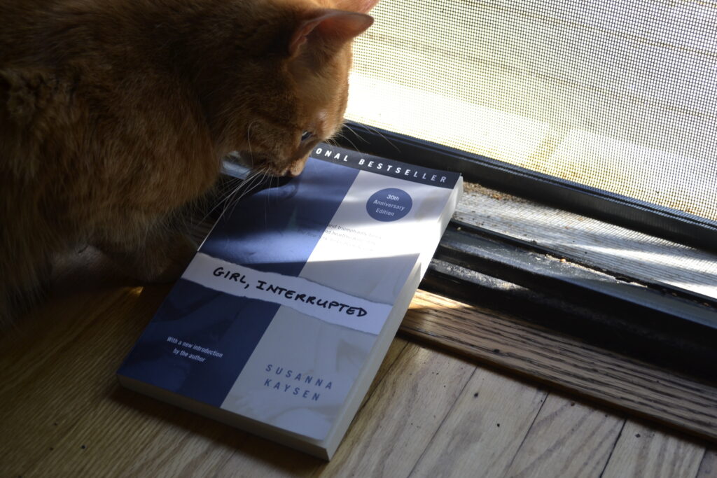 An orange tabby cat presses her nose against the cover of Girl, Interrupted.