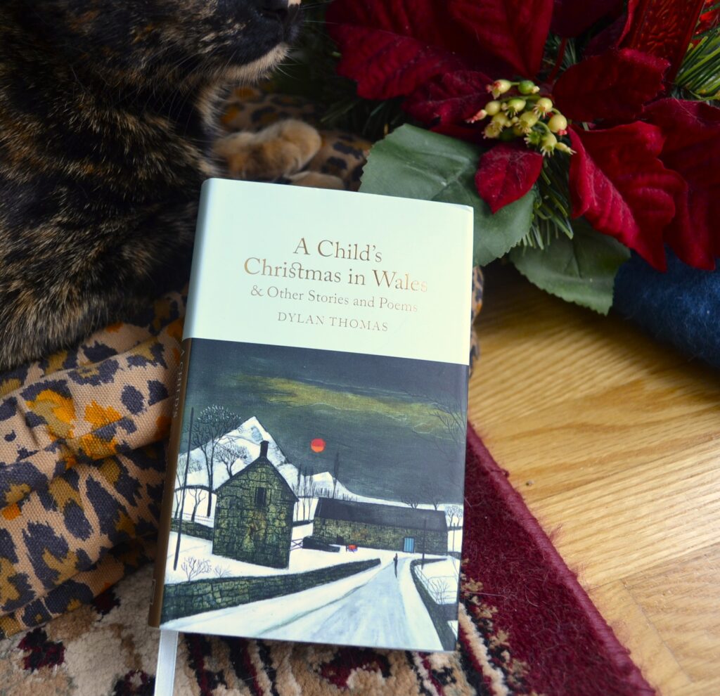 A Child's Christmas in Wales and Other Stories and Poems in a small hardcover book by Dylan Thomas. The cover features a painting of a stone house in winter.