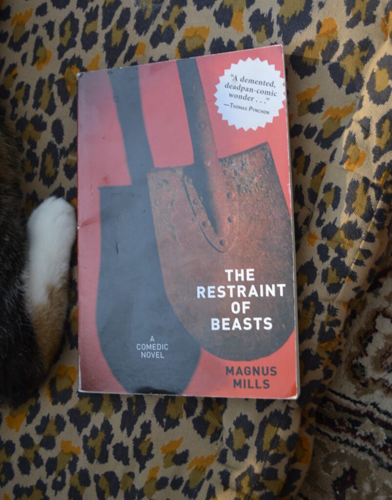 The Restraint of Beasts by Magnus Mills is a red paperback book with a rusty shovel on the cover. A white paw pushes against one side.