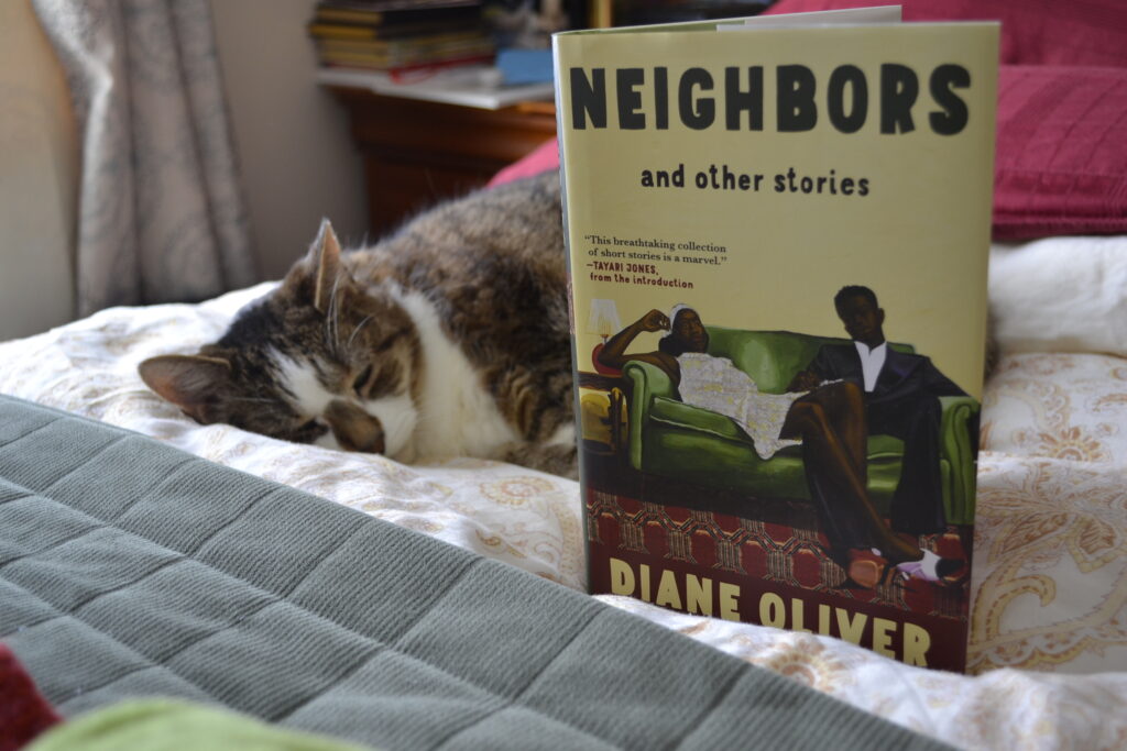 A tabby cat sleeps heavily behind a copy of Diane Oliver's Neighbors and Other Stories.