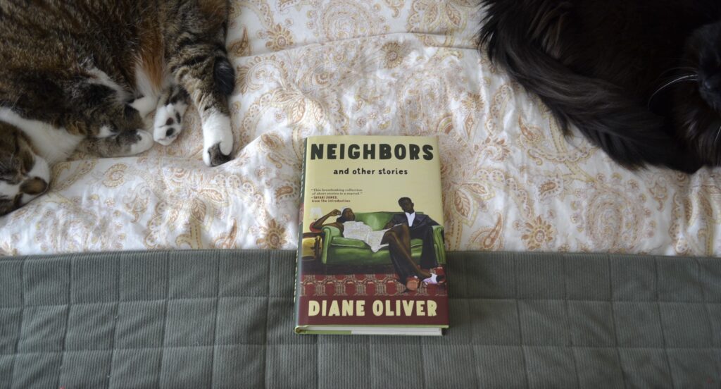 A black cat and a tabby cat sit on either side of Diane Oliver's Neighbors.