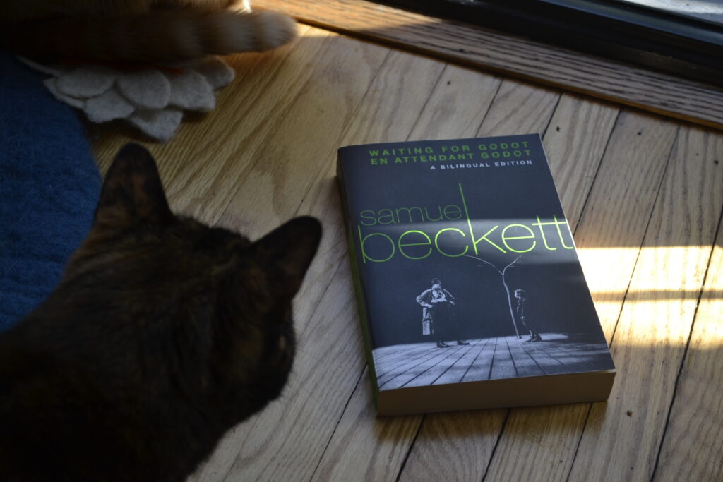 A copy of Beckett's Waiting for Godot features line-green text and a black-and-white picture of a man looking at a child beneath a bare tree on an otherwise empty stage.