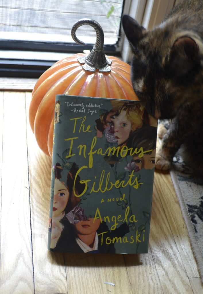 A tortoiseshell cat rubs the top edge of a green book that leans against an orange glass pumpkin.