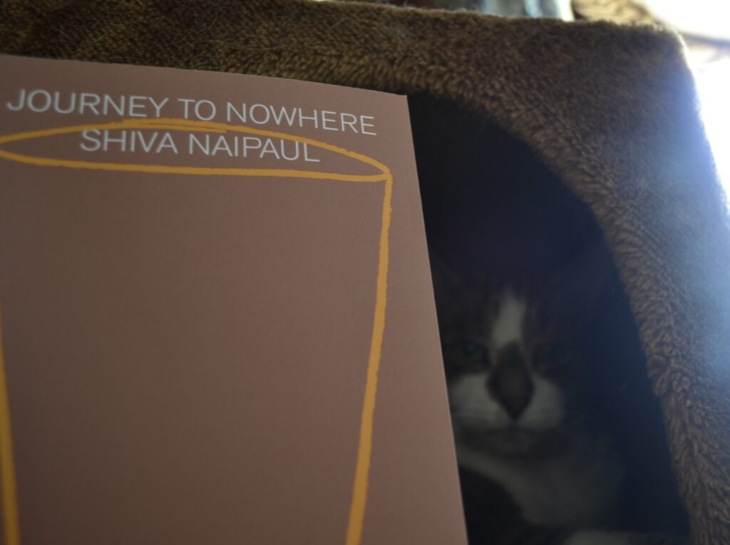The book Journey to Nowhere by Shive Naipaul is a brown softcover book with white text and a pale-orange line drawing of a cup on the cover.